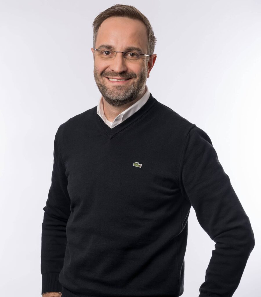 Mann mit Brille und dunklem Pullover lächelt in die Kamera – professionelles Porträtfoto für das HotSpring Team