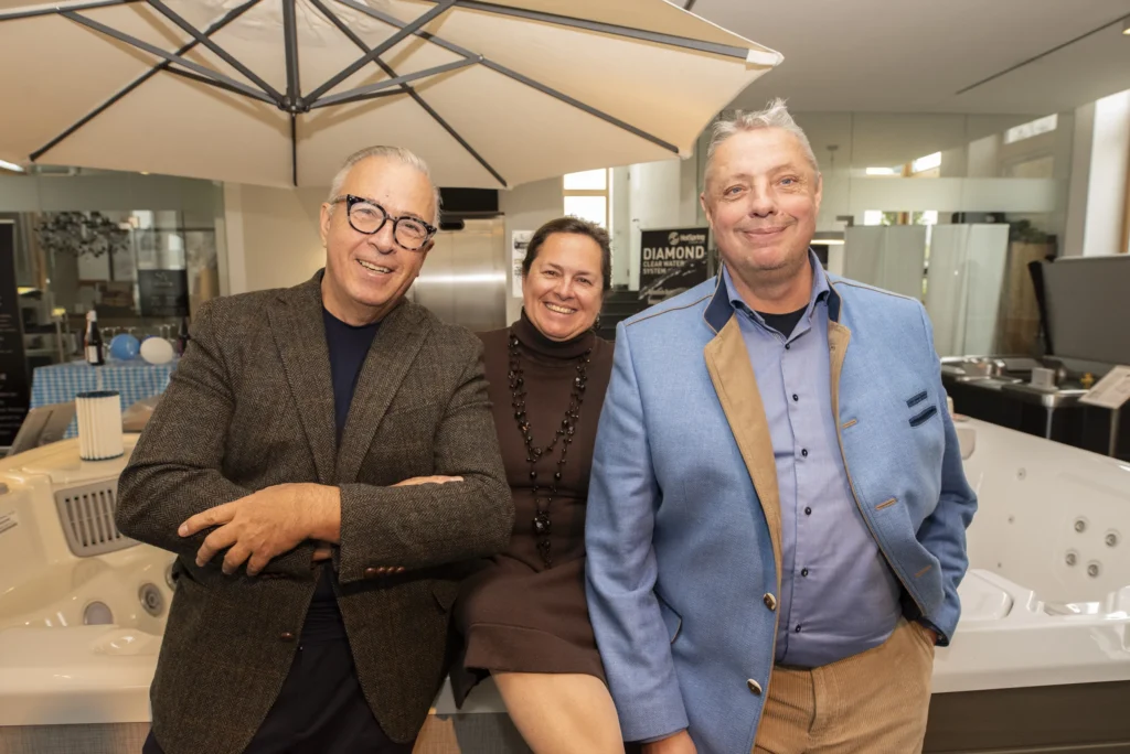 Besuchergruppe in einem HotSpring Showroom bei einer Hausmesse, entspannt vor ausgestellten Whirlpools stehend und in freundlicher Event-Atmosphäre – HotSpring